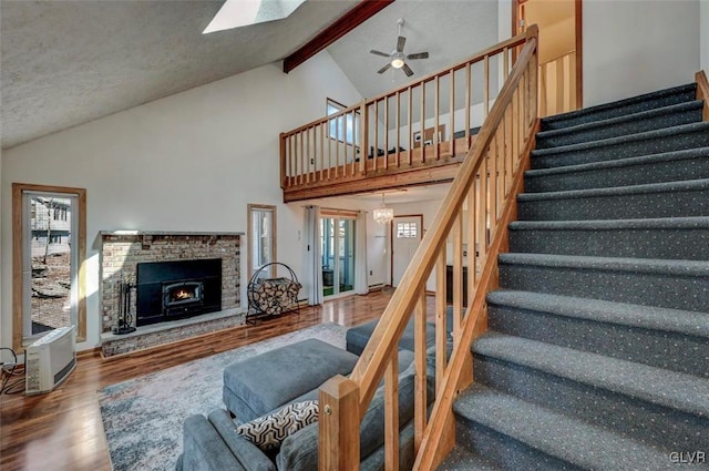 living area featuring ceiling fan, beamed ceiling, stairs, a lit fireplace, and wood finished floors