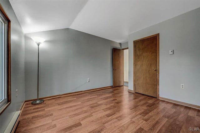 spare room featuring baseboard heating, baseboards, lofted ceiling, and wood finished floors