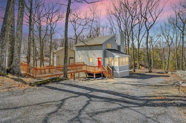 view of front facade featuring a deck, a chimney, and a shingled roof