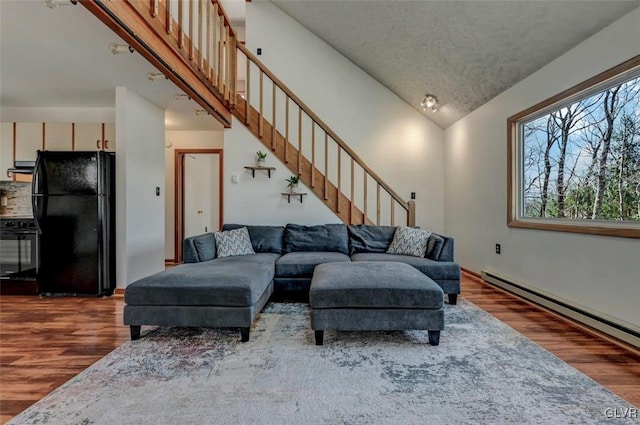 living room featuring stairs, wood finished floors, a baseboard heating unit, and high vaulted ceiling