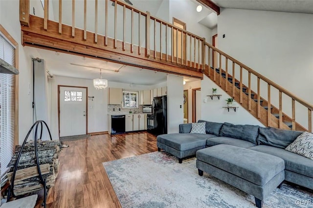 living room featuring wood finished floors, high vaulted ceiling, stairs, beamed ceiling, and a notable chandelier