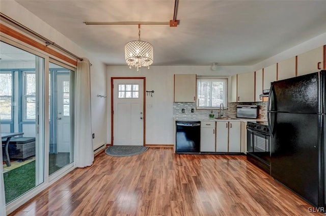 kitchen featuring light wood finished floors, an inviting chandelier, decorative backsplash, black appliances, and light countertops