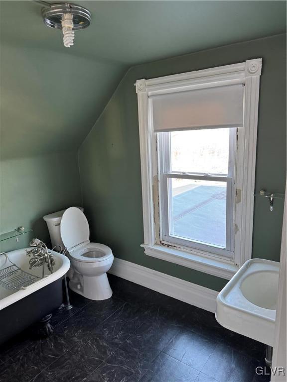 bathroom featuring lofted ceiling, toilet, baseboards, and a freestanding bath