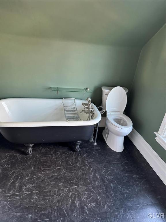 full bath with toilet, marble finish floor, lofted ceiling, baseboards, and a freestanding bath