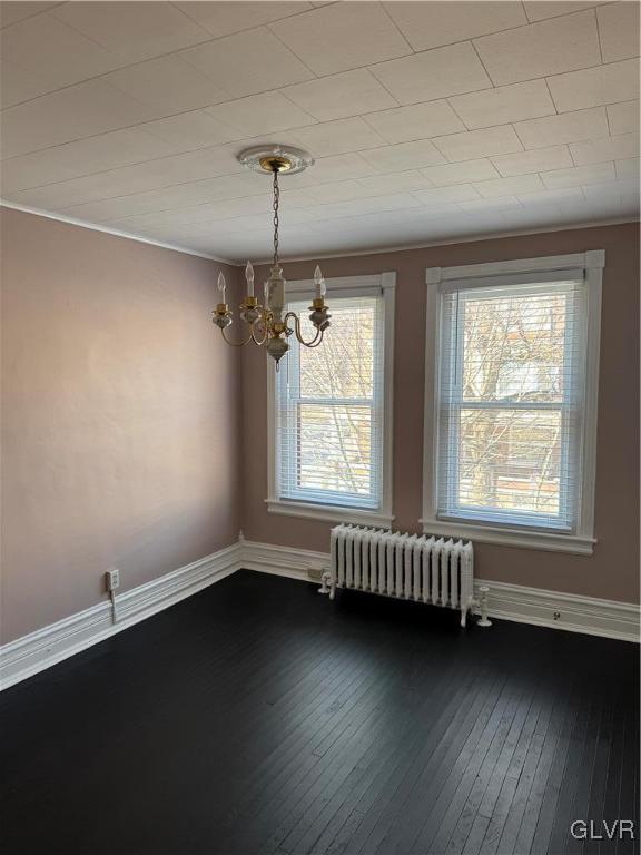 unfurnished dining area featuring baseboards, dark wood-type flooring, a chandelier, and radiator heating unit