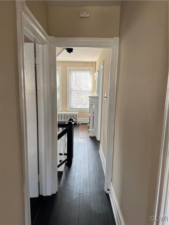 hallway with dark wood-type flooring, radiator heating unit, and baseboards