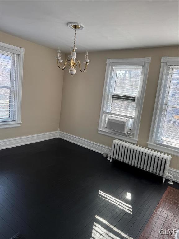 empty room featuring baseboards, radiator, an inviting chandelier, and a healthy amount of sunlight