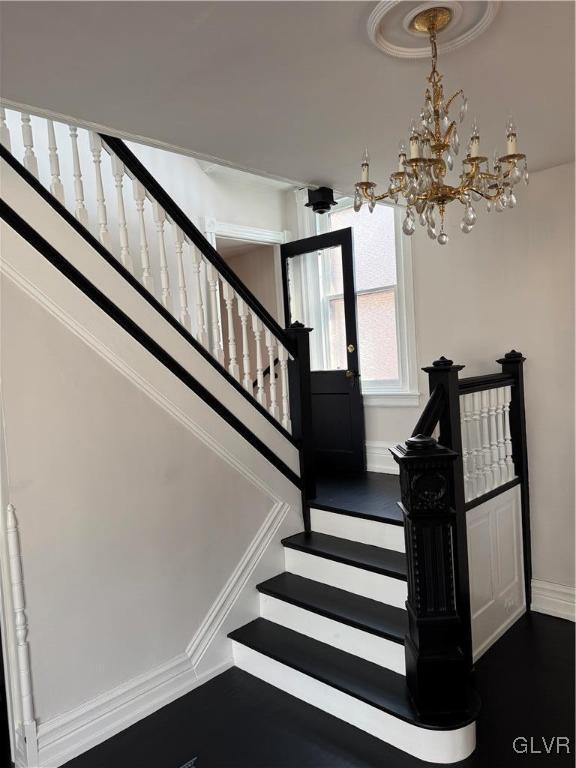 stairs featuring a notable chandelier, wood finished floors, and baseboards