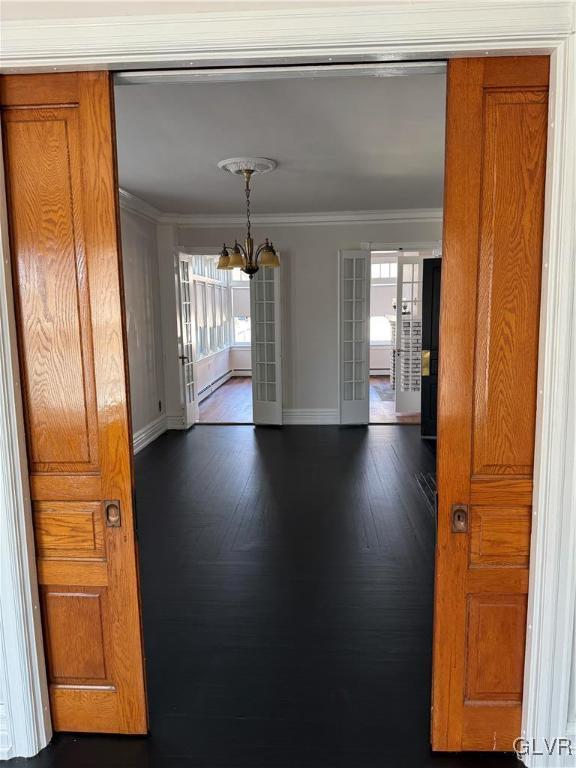 empty room with dark wood-type flooring, a notable chandelier, french doors, crown molding, and baseboards