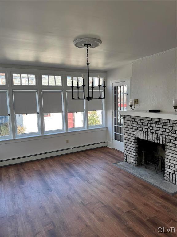 unfurnished living room with a notable chandelier, dark wood-style flooring, a brick fireplace, and a baseboard radiator