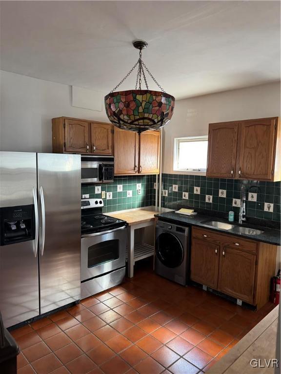 kitchen with washer / dryer, a sink, stainless steel appliances, dark countertops, and backsplash