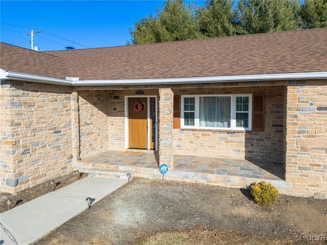 view of exterior entry with covered porch, roof with shingles, and brick siding