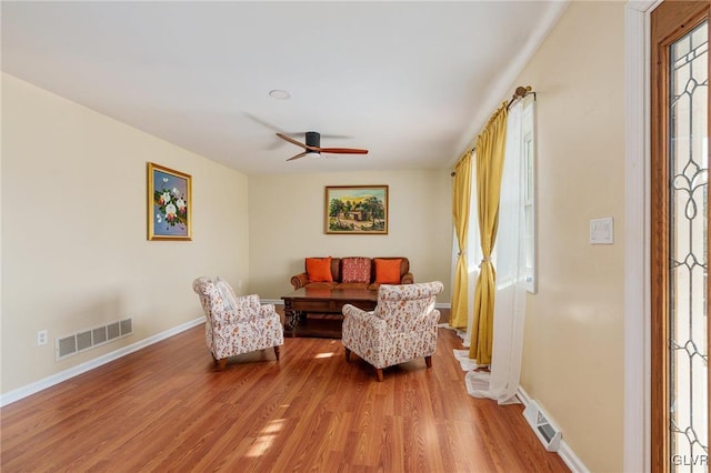 living area featuring light wood finished floors, visible vents, baseboards, and ceiling fan