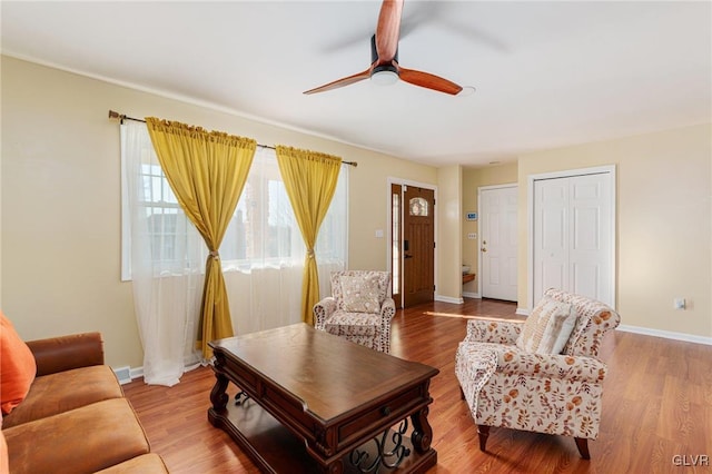 living area featuring wood finished floors, baseboards, and ceiling fan