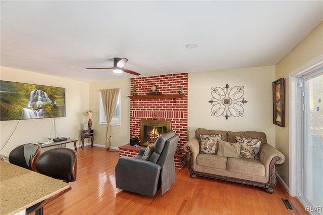 living area with visible vents, wood finished floors, baseboards, a brick fireplace, and ceiling fan