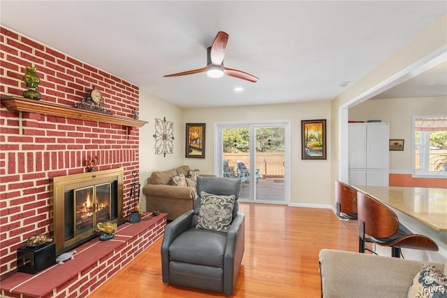 living room with a fireplace, light wood-style floors, baseboards, and ceiling fan