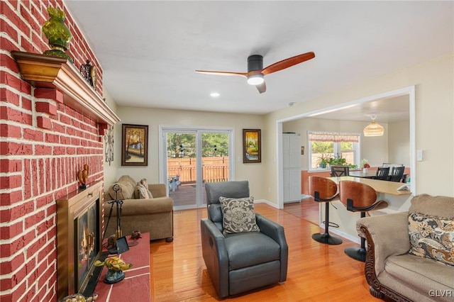 living area with a brick fireplace, baseboards, light wood-type flooring, and ceiling fan