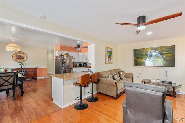 living room with light wood-style flooring, a ceiling fan, and baseboards