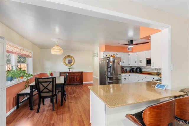 kitchen featuring tasteful backsplash, appliances with stainless steel finishes, a peninsula, white cabinets, and light wood finished floors