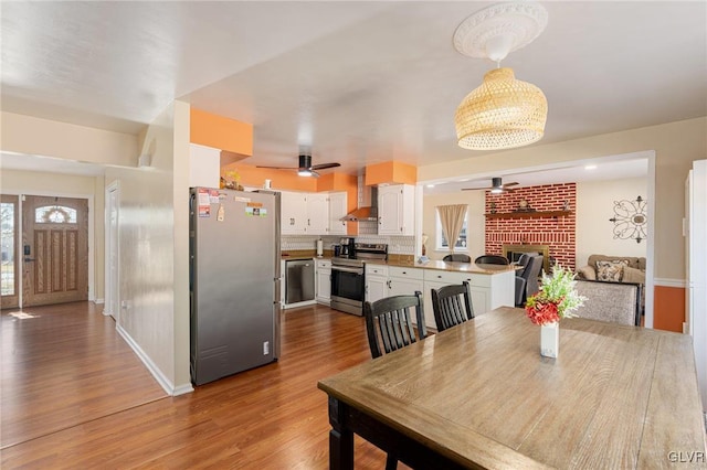 dining room featuring a fireplace, wood finished floors, baseboards, and ceiling fan