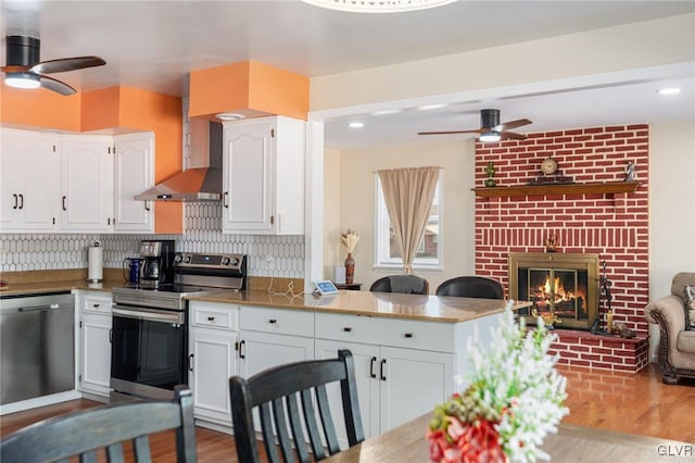 kitchen with appliances with stainless steel finishes, white cabinetry, wall chimney exhaust hood, and a ceiling fan