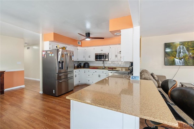 kitchen with light stone counters, a peninsula, ceiling fan, stainless steel appliances, and white cabinets