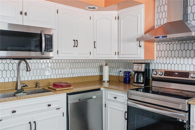 kitchen with a sink, stainless steel appliances, white cabinets, wall chimney range hood, and tasteful backsplash