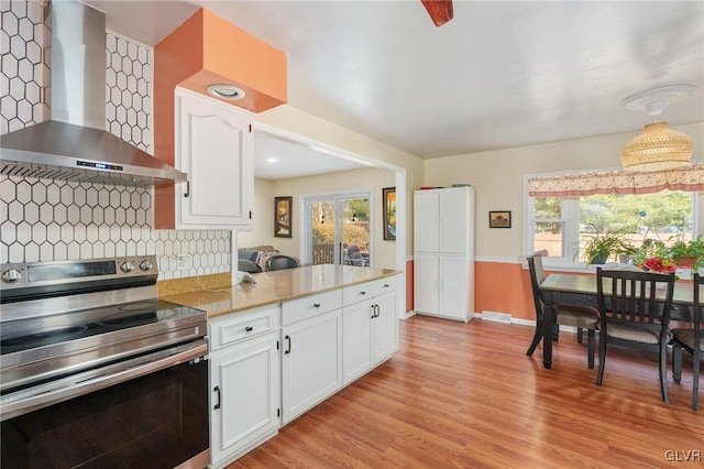 kitchen featuring electric range, decorative backsplash, light wood-style floors, white cabinetry, and wall chimney range hood