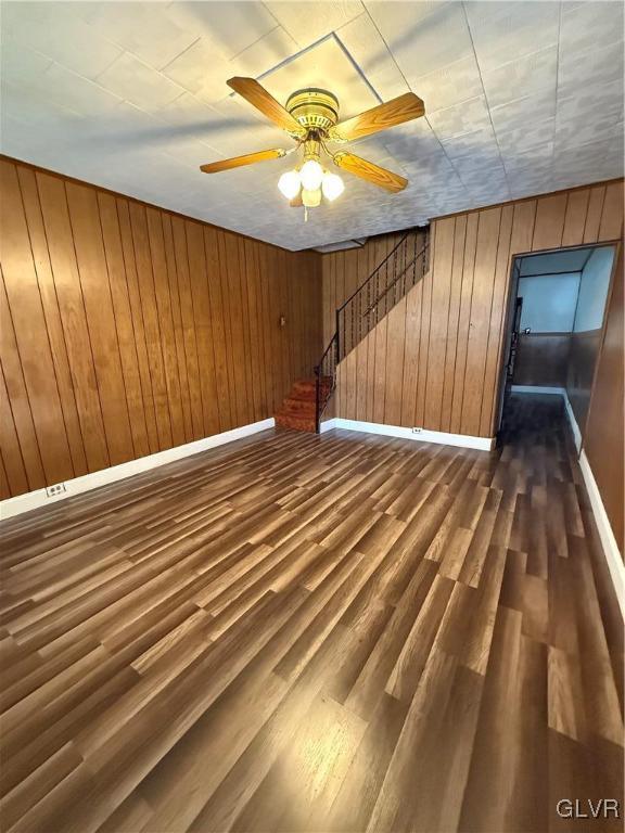 interior space featuring baseboards, wooden walls, ceiling fan, and dark wood-style flooring