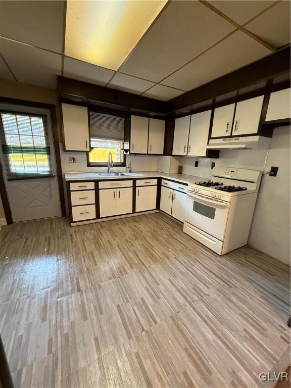 kitchen featuring under cabinet range hood, white range with gas cooktop, light wood-style floors, a paneled ceiling, and a sink