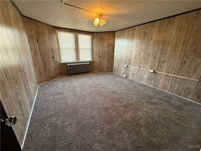 carpeted empty room featuring wooden walls and radiator heating unit