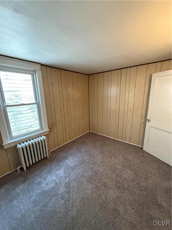 unfurnished room with wooden walls, radiator heating unit, and dark carpet