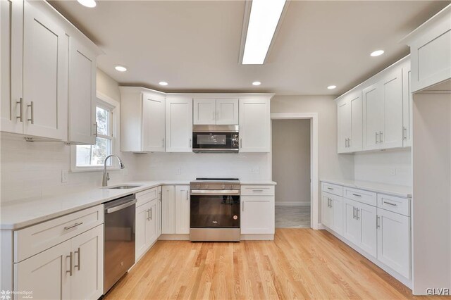 kitchen with a sink, appliances with stainless steel finishes, light wood-style flooring, and white cabinetry