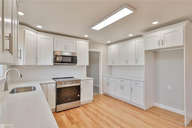 kitchen featuring recessed lighting, stainless steel appliances, light wood-style floors, white cabinetry, and a sink