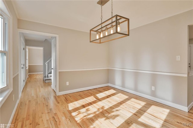 unfurnished dining area with stairway, a notable chandelier, light wood-style floors, and baseboards