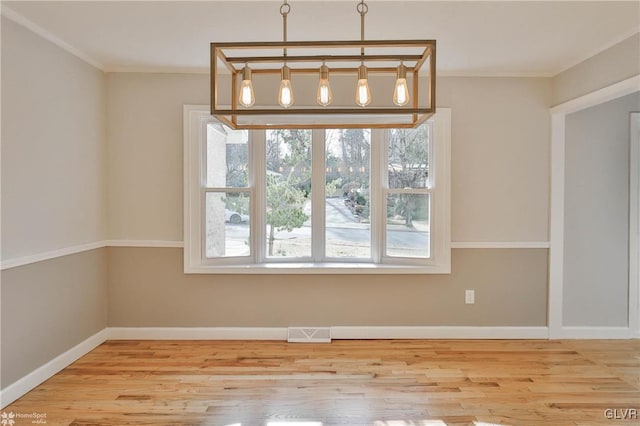 unfurnished dining area featuring baseboards, wood finished floors, visible vents, and ornamental molding