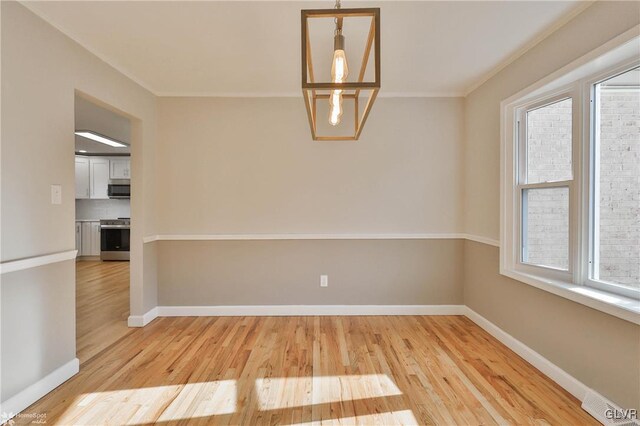 unfurnished dining area featuring crown molding, light wood-style flooring, a notable chandelier, and baseboards