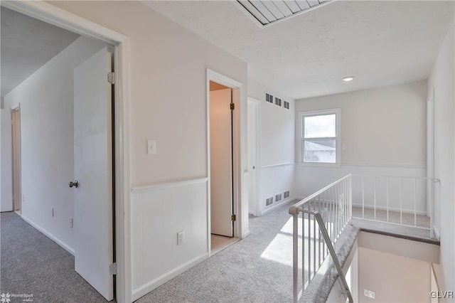 hall featuring an upstairs landing, visible vents, wainscoting, and carpet