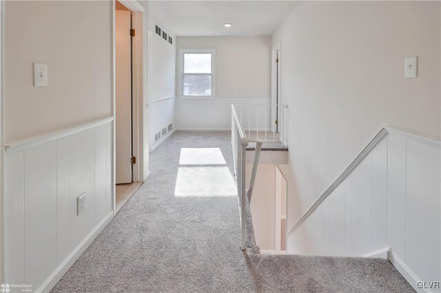 corridor featuring visible vents, carpet, a wainscoted wall, and a decorative wall