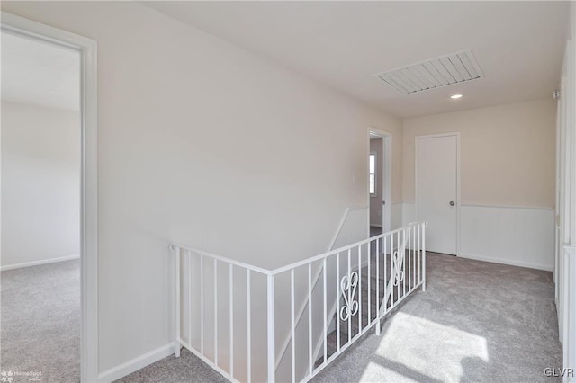 hall featuring carpet flooring, an upstairs landing, visible vents, and baseboards