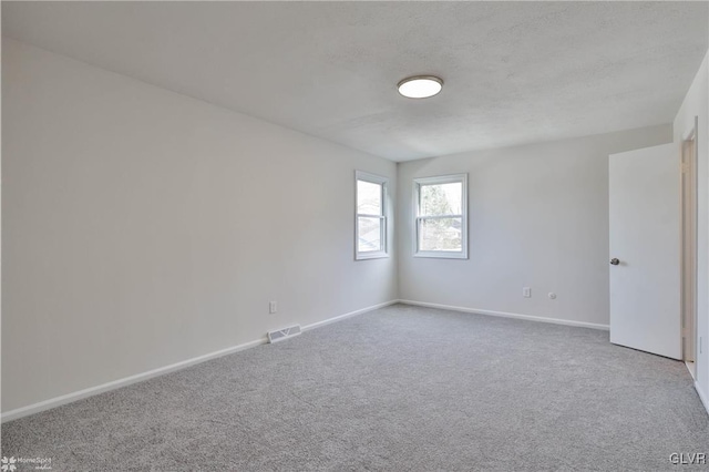 carpeted spare room with visible vents, baseboards, and a textured ceiling