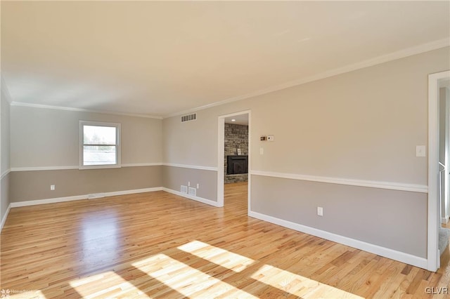 spare room with light wood-type flooring, visible vents, a large fireplace, crown molding, and baseboards