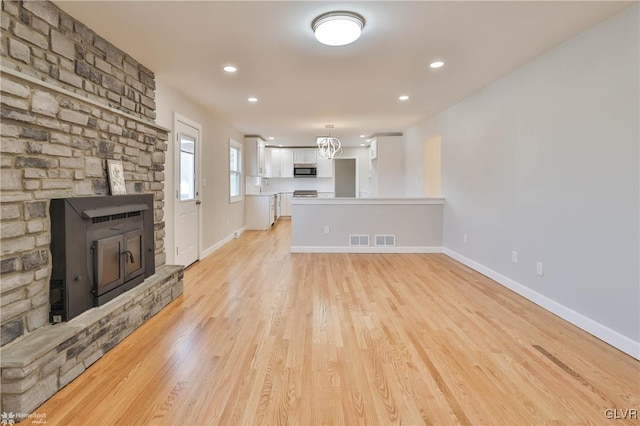 unfurnished living room with visible vents, light wood-style flooring, a wood stove, and baseboards