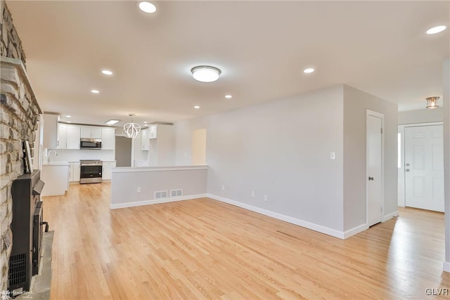 unfurnished living room featuring light wood-type flooring, visible vents, a sink, recessed lighting, and baseboards