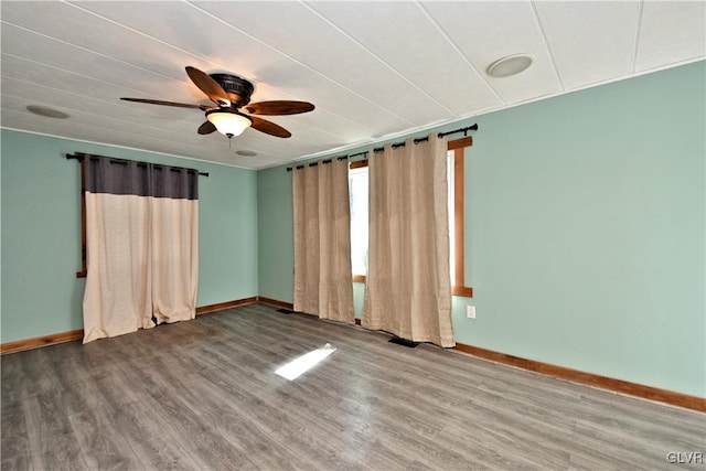 empty room with visible vents, wood finished floors, baseboards, and ceiling fan