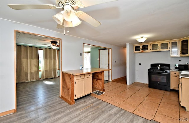 kitchen featuring ceiling fan, black appliances, light countertops, glass insert cabinets, and light wood-type flooring