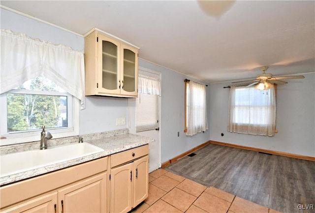 kitchen with a sink, light tile patterned flooring, light countertops, glass insert cabinets, and ceiling fan