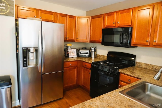 kitchen with light stone counters, brown cabinets, wood finished floors, black appliances, and a sink