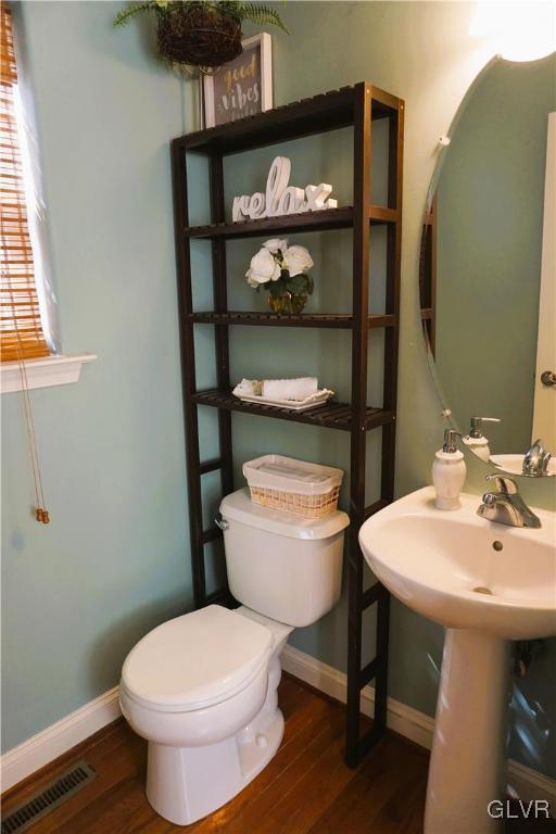 half bathroom with toilet, wood finished floors, visible vents, and baseboards