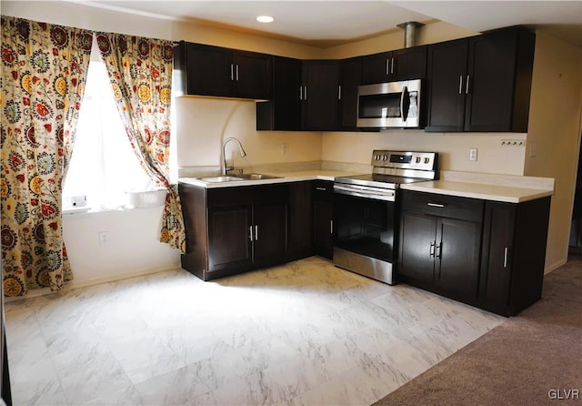 kitchen with stainless steel appliances, dark cabinetry, light countertops, and a sink